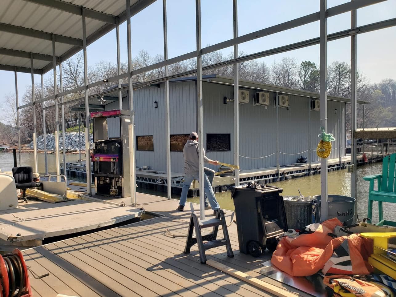 Covered lake dock and boathouse area under construction on Grand Lake with metal framing, storage items, and workers on the deck