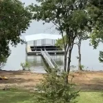 Covered boat dock with walkway extending into Grand Lake, framed by trees on the shoreline in Grand Lake, Oklahoma